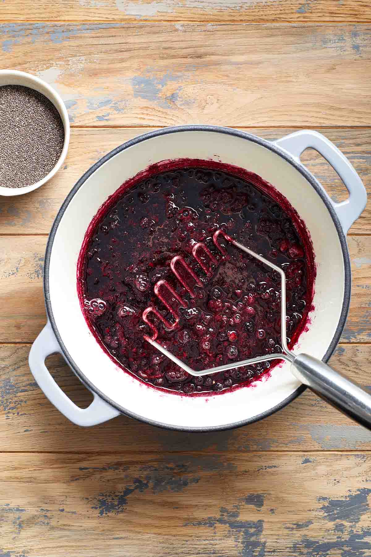 Mashed berries in a pot with a potato masher.