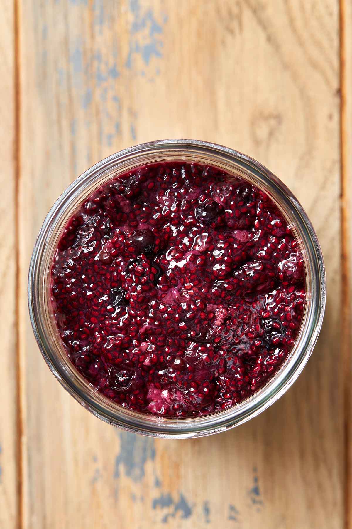 Overhead view of chia seed jam in a glass jar on a wooden table.