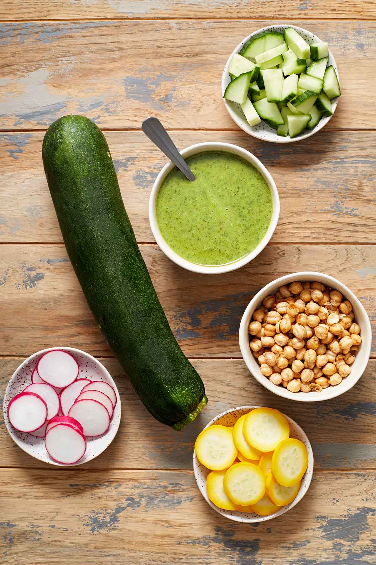 Ingredients to make zucchini noodle bowls arranged on a wooden table.