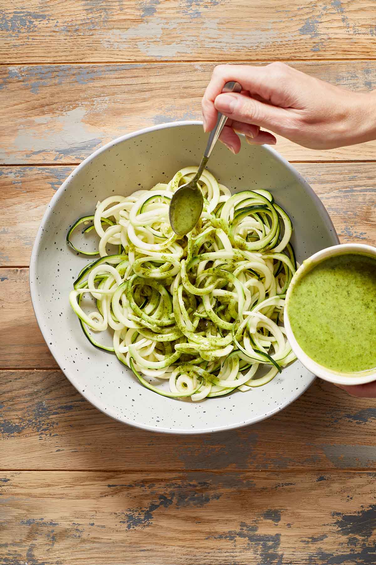 Zucchini noodles in a large bowl with jalapeño vinaigrette being drizzled over them with a spoon.