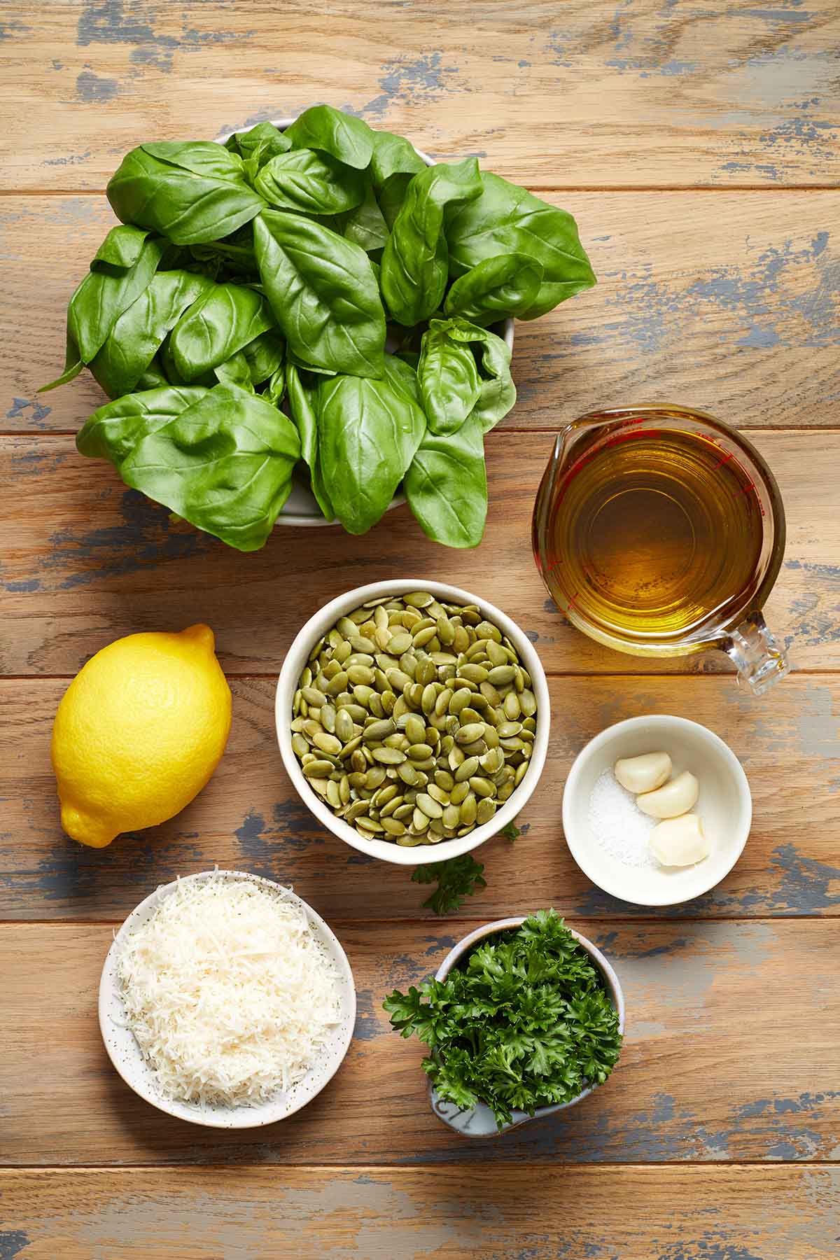 Ingredients to make pumpkin seed pesto arranged individually on a wooden table.