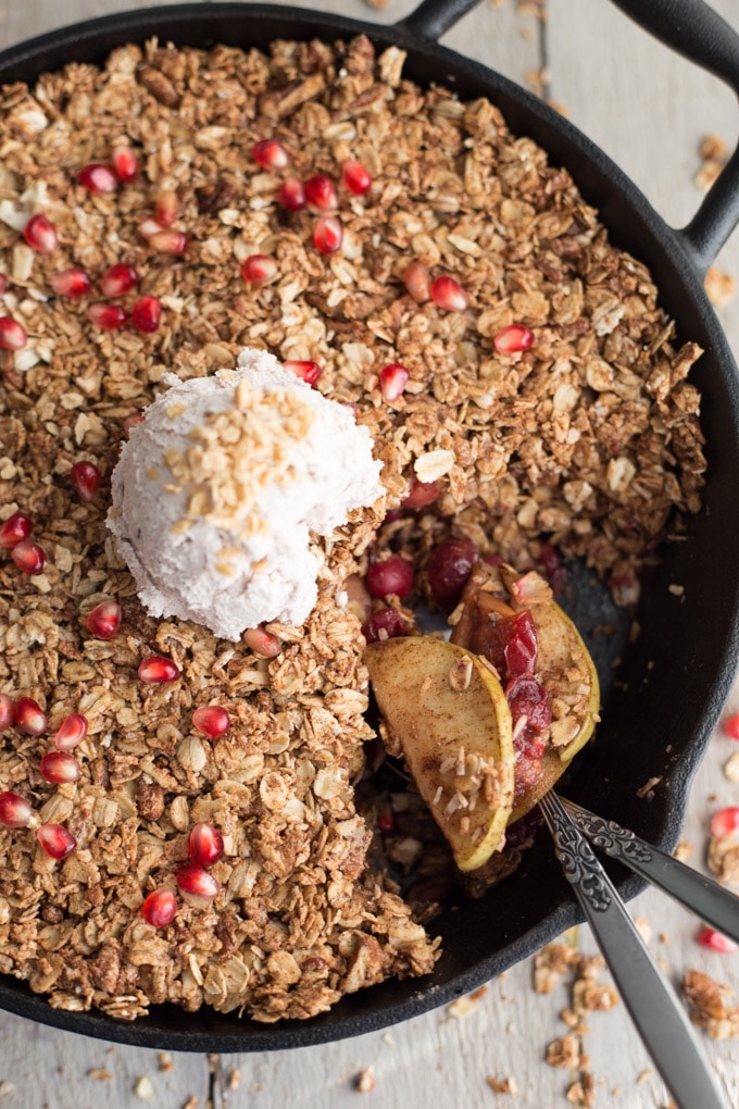 Overhead view of apple cranberry crisp topped with coconut whip in a black cast iron pan.