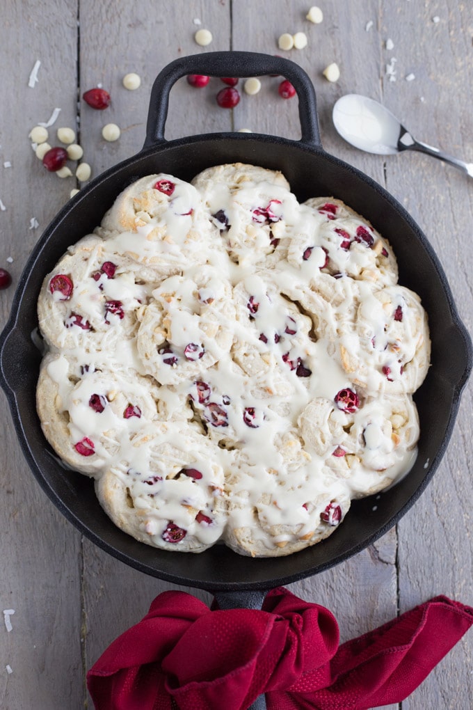 Older image of cranberry rolls in a cast iron skillet and topped with white chocolate.