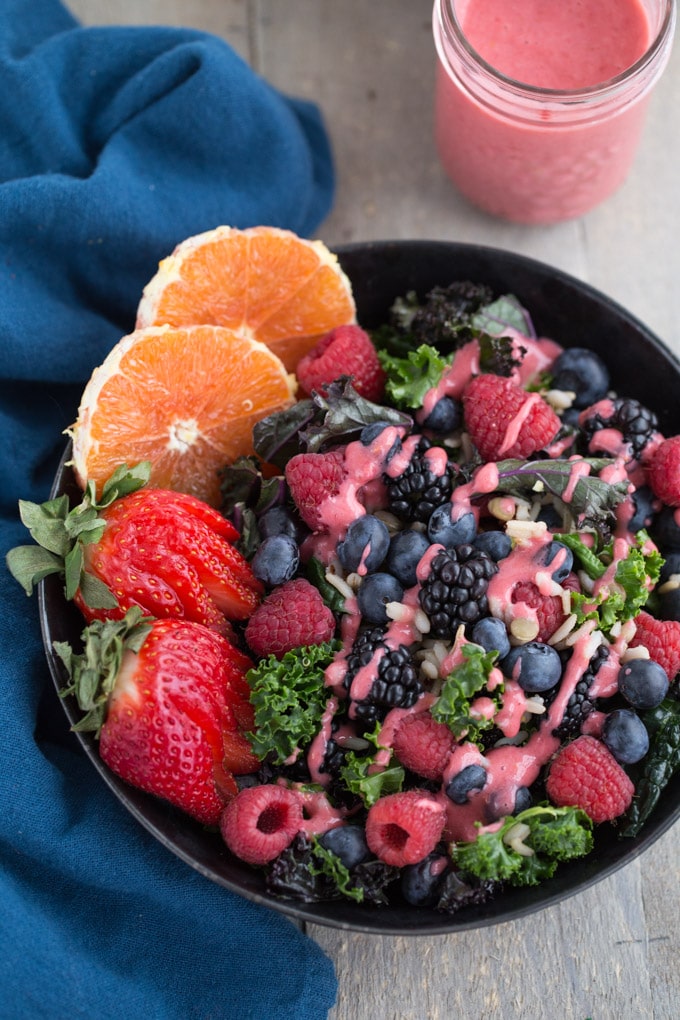 Berry Citrus Kale Salad in a black bowl with a jar of Raspberry Vinaigrette on the side.