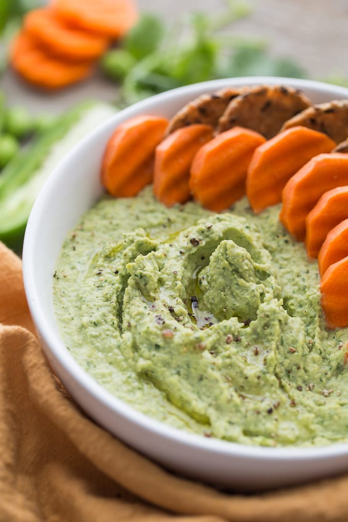 Older image of edamame hummus - up close in a white bowl with carrots and crackers in the bowl.