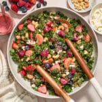 Kale berry citrus salad in a large serving bowl with wooden serving spoons inserted into it.