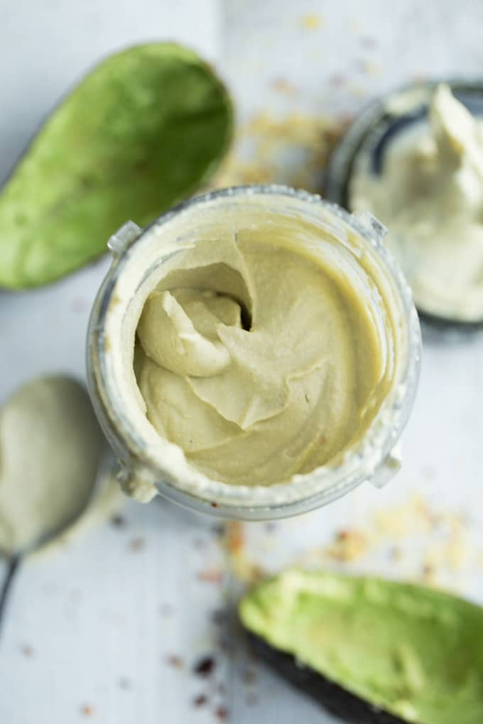 Overhead view of avocado cream sauce in a mason jar on a white surface.