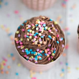 Overhead view of Flourless Ricotta Cupcakes topped with Chocolate Coconut Cream and sprinkles on a white wooden surface.