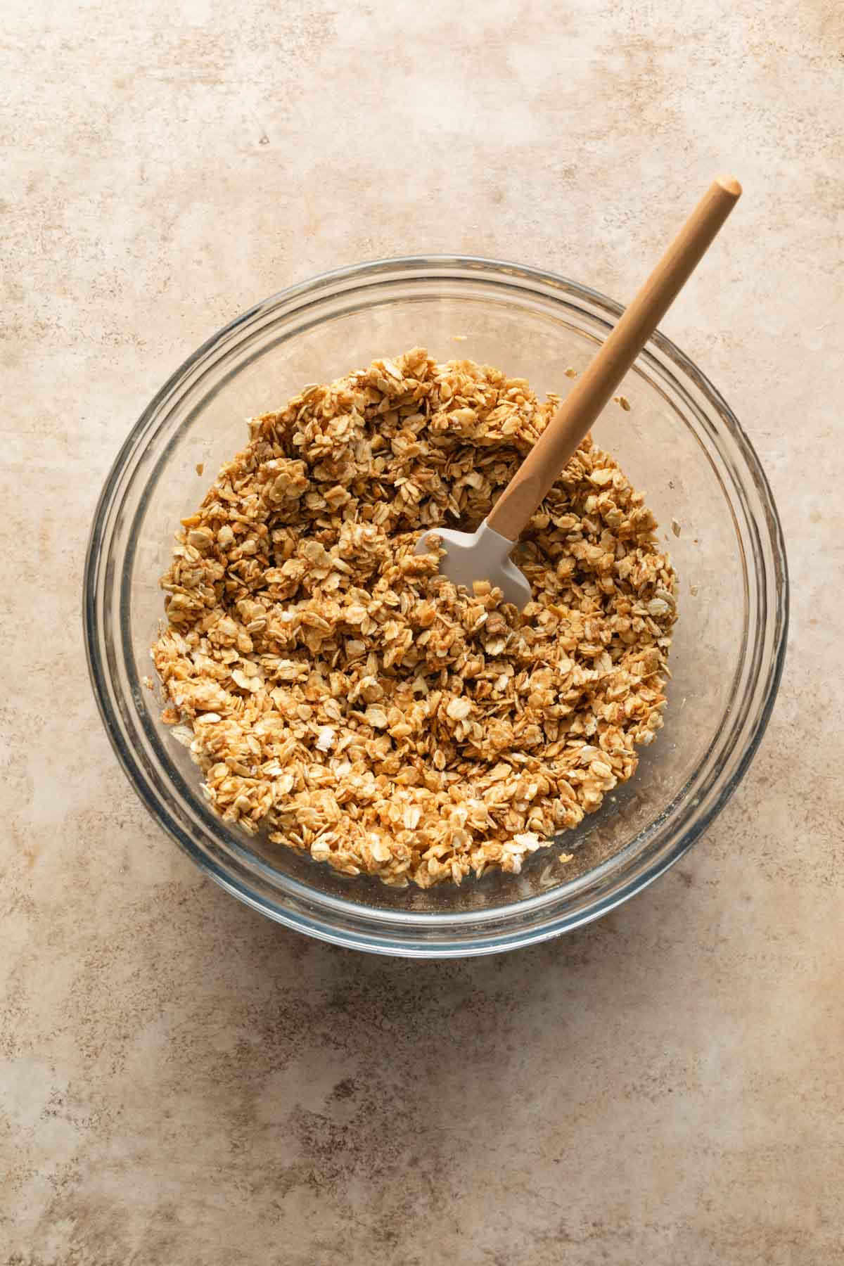 Granola mixed together in a glass bowl with a spatula.