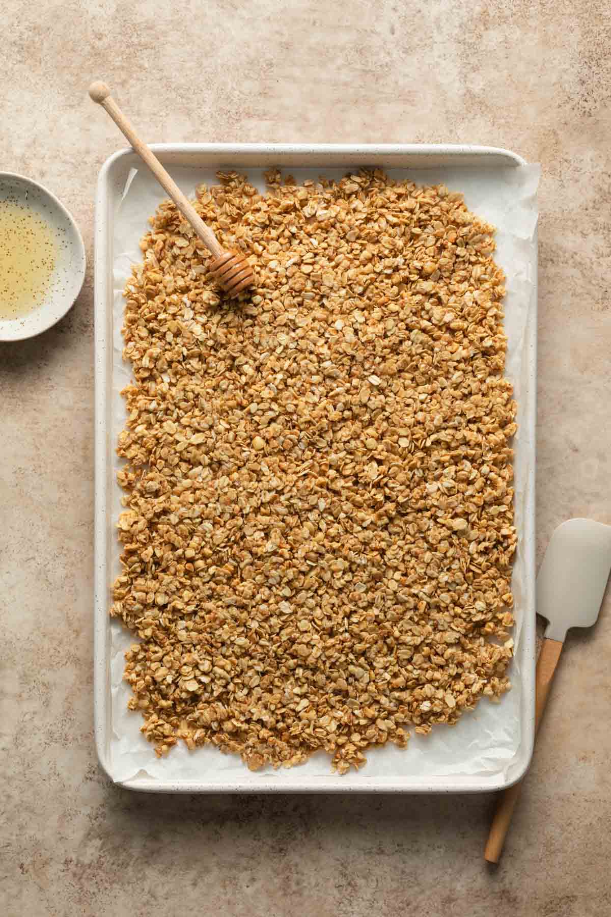 Granola mixture spread out on a white baking sheet.