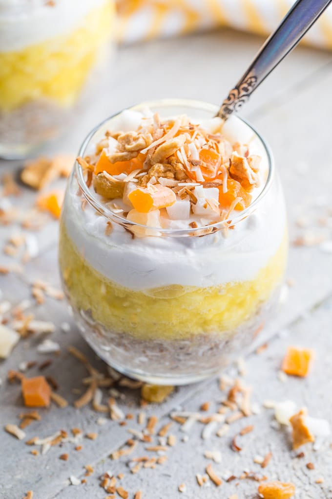 Older photo of pineapple coconut chia pudding in a glass with a spoon on a wooden surface.