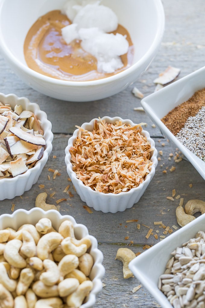 Overhead view of ingredients for Coconut Cashew Crunch Grain-Free Granola in individual dishes and spread out on a wooden surface.