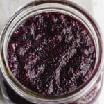 Overhead close up of blueberry chia jam in a wide mouth glass jar.