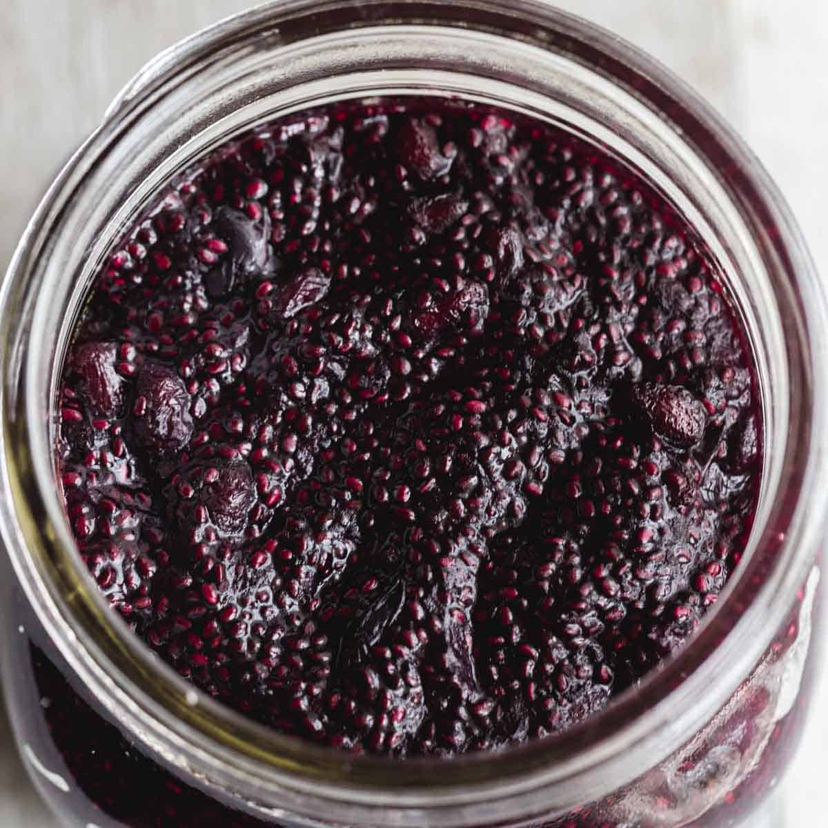 Overhead close up of blueberry chia jam in a wide mouth glass jar.