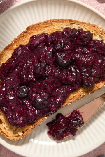 Blueberry lemon chia jam spread on a slice of toast with a knife on the side.