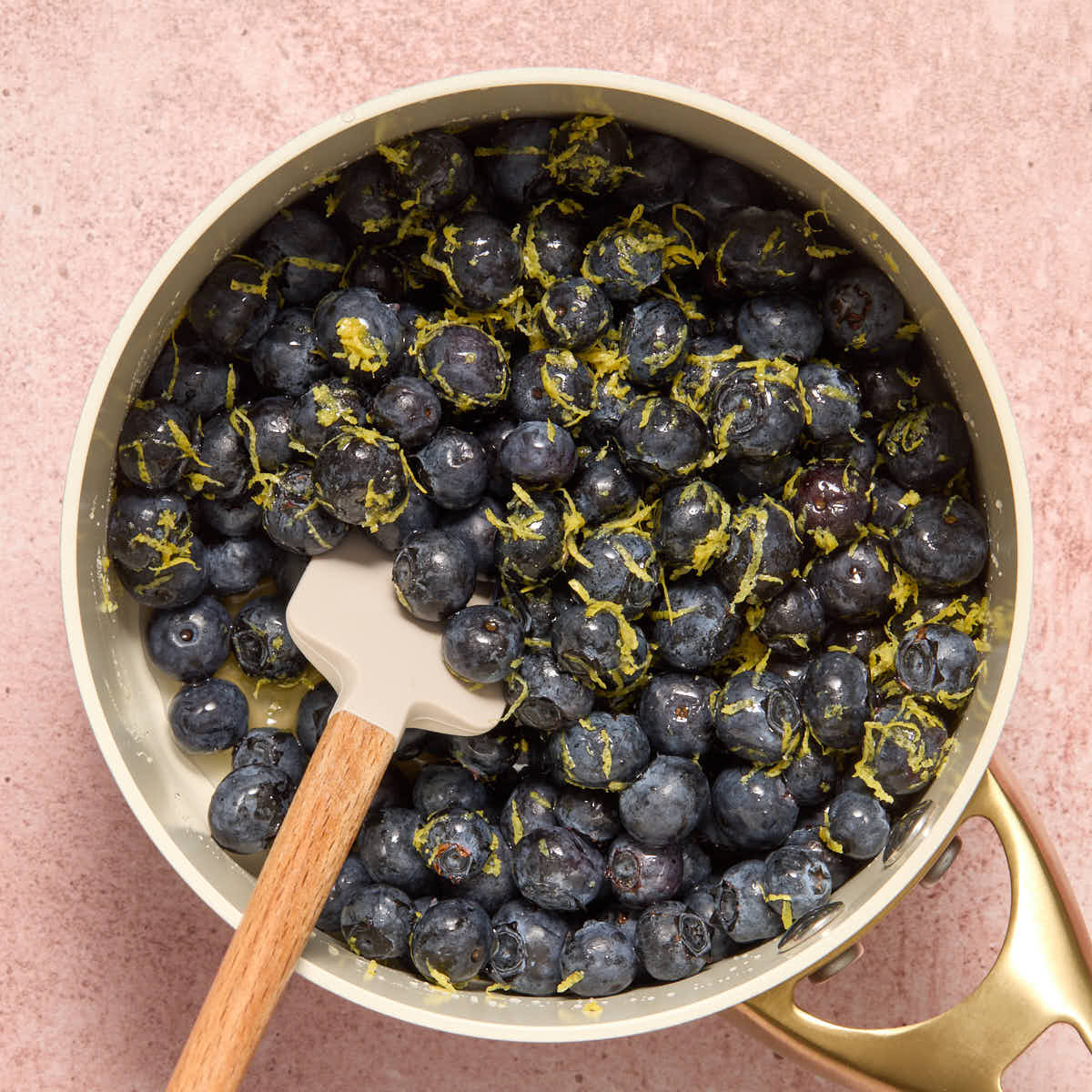 Blueberries stirred together with lemon zest, juice and maple syrup with a spatula inserted into it.