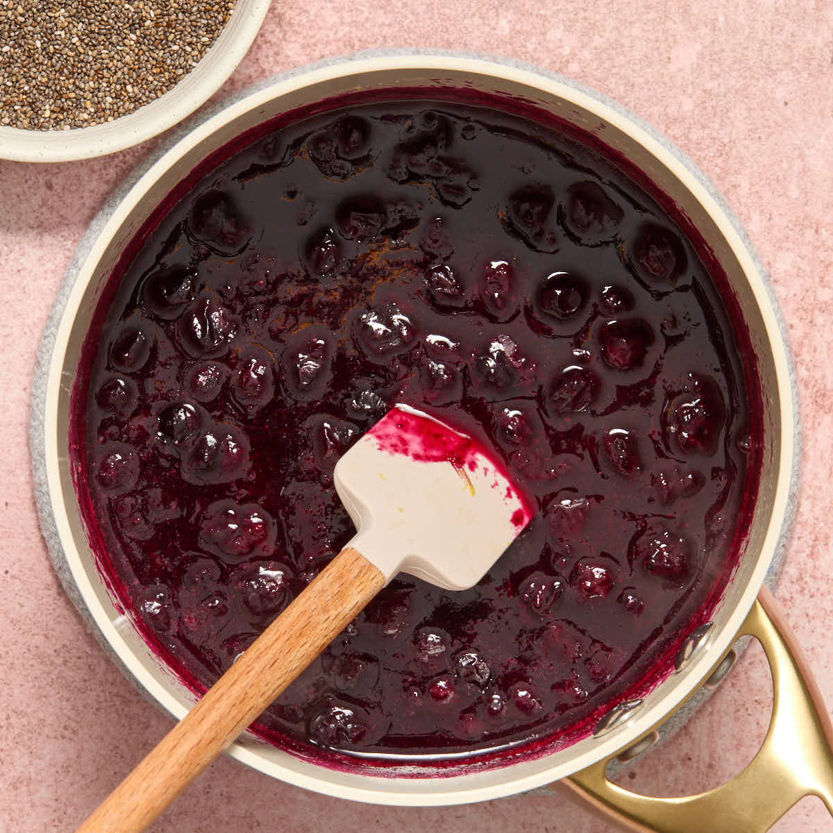 Cooked blueberry mixture in a small sauce pan with chia seeds on the side.