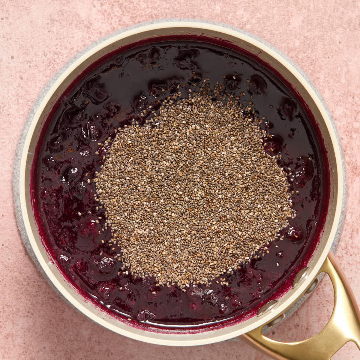 Chia seeds added on top of the cooked blueberries in a sauce pan.