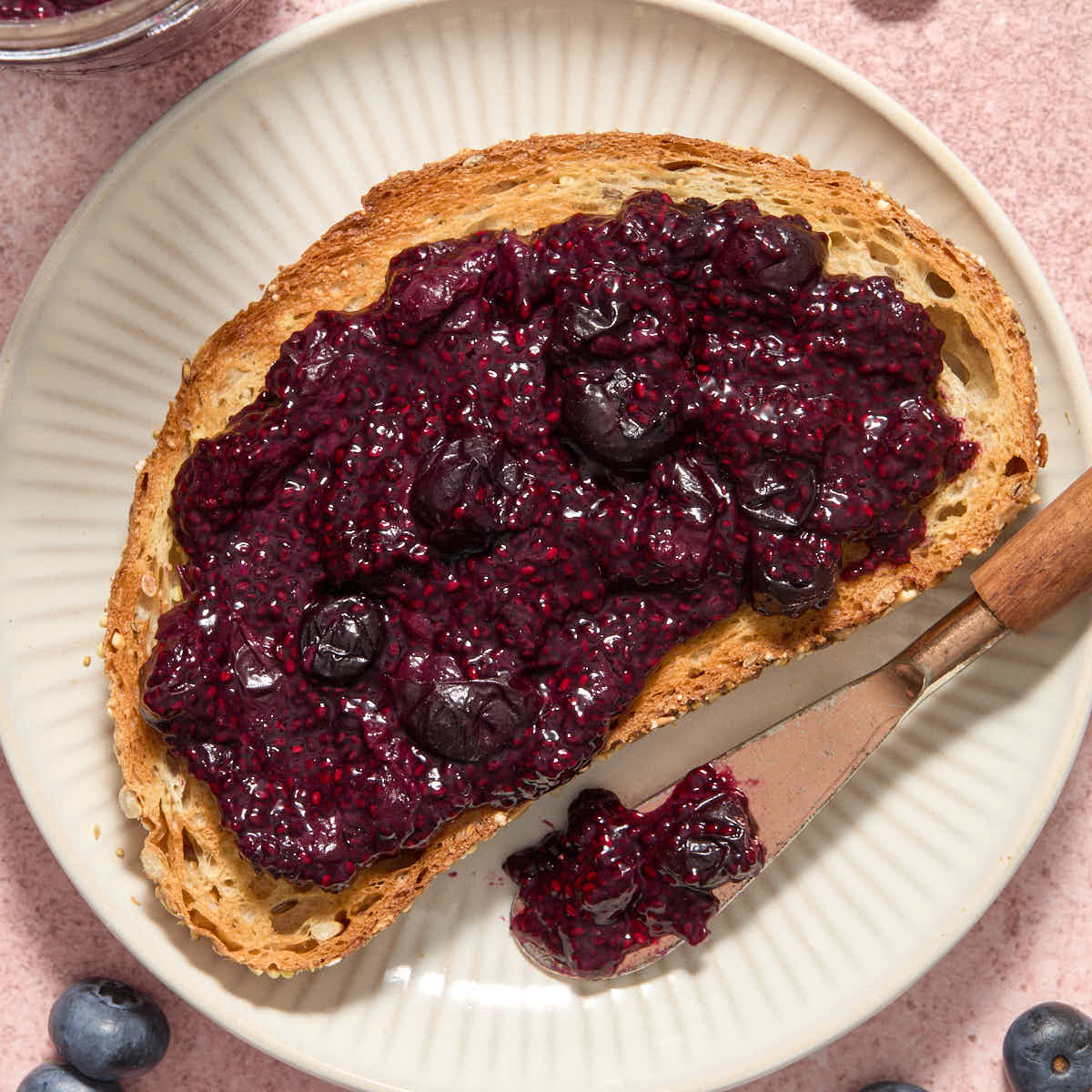 Blueberry lemon chia jam spread on a slice of toast with a knife on the side.