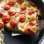 Close up view of a slice of cheese, tomato and arugula quiche in a black skillet.