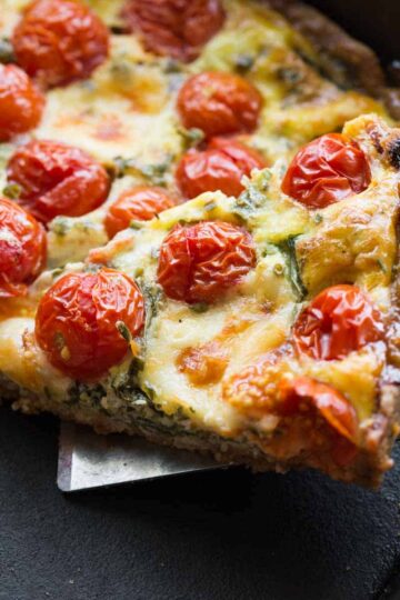 Close up view of a slice of cheese, tomato and arugula quiche in a black skillet.