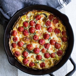 Overhead view of Tomato, Arugula and Mozzarella Quiche in a cast iron pan on a wooden surface.