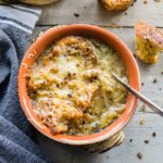 Overhead of a bowl of French onion soup with a napkin and croutons next to it.
