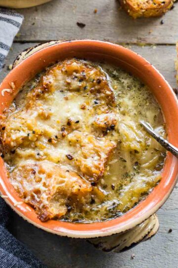 Overhead of a bowl of French onion soup with a napkin and croutons next to it.