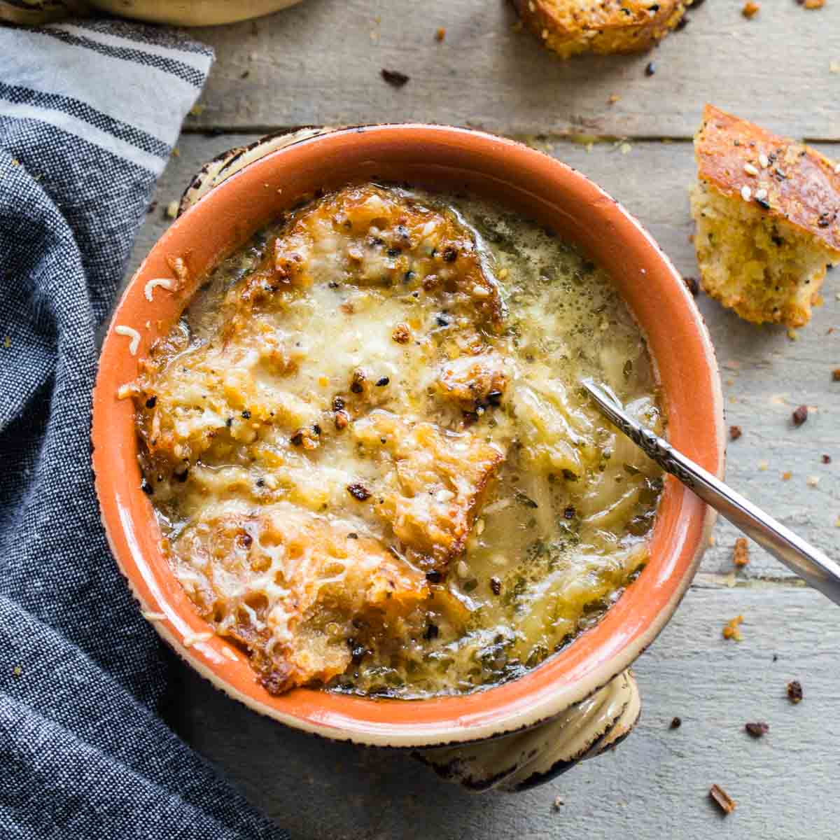 Overhead of a bowl of French onion soup with a napkin and croutons next to it.
