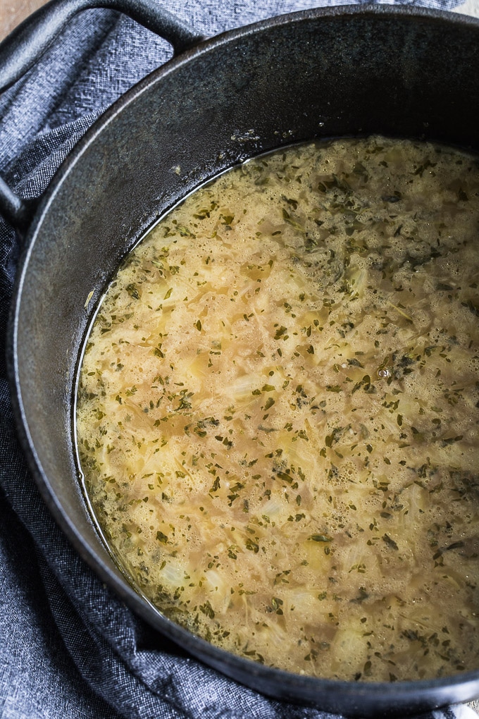 Overhead view of cooked Easy Bone Broth French Onion Soup in a black cast iron pot.
