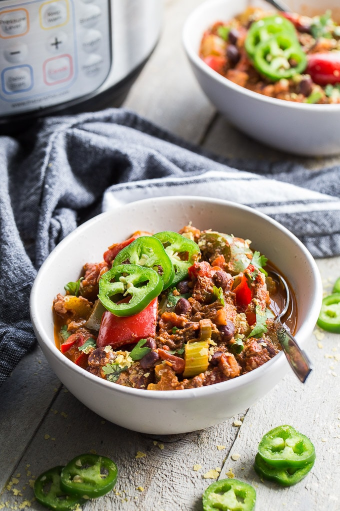 Up-close side view of Instant Pot Spicy Vegan Chili in a white bowl on a wooden surface with the Instant Pot and another bowl of chili in the background.