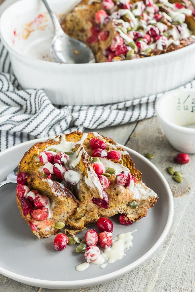 Side view of a piece of Cranberry Pumpkin French Toast Bake on a grey plate with the baking dish of french toast in the background.
