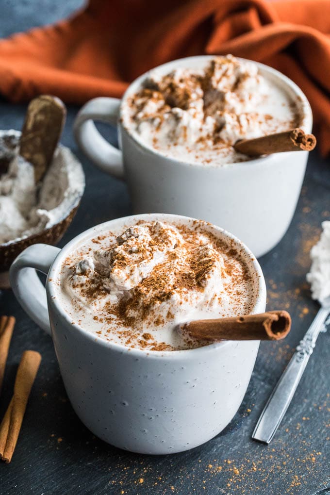 Two Pumpkin Spice Collagen Lattes topped with coconut whip, pumpkin spice and a cinnamon stick.