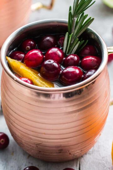 Cranberry orange kombucha mule with cranberries and a sprig of rosemary on top.