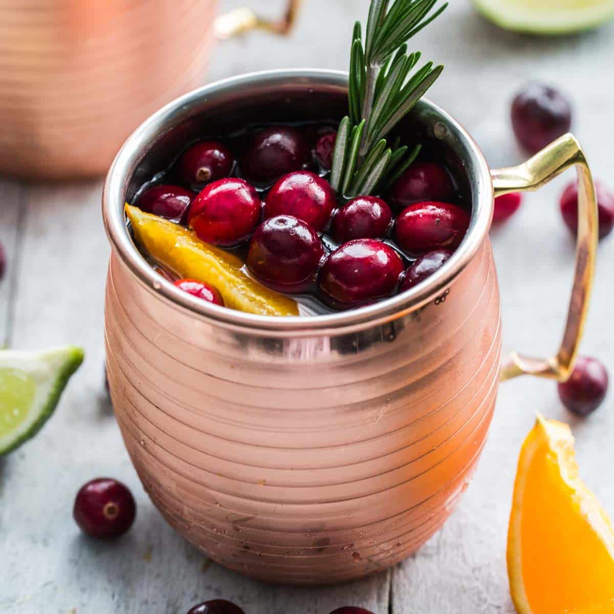 Cranberry orange kombucha mule with cranberries and a sprig of rosemary on top.