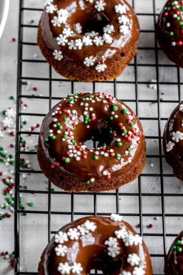 Overhead of mini gingerbread donuts topped with sprinkles and placed on a black wire rack.