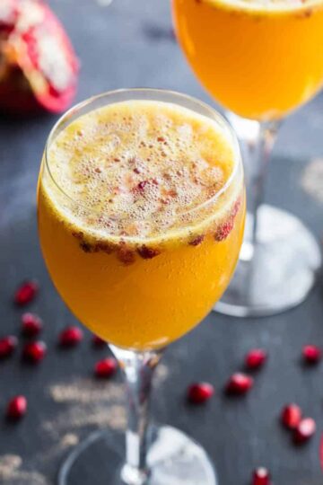 Ginger beer mimosas in wine glasses with pomegranate arils.