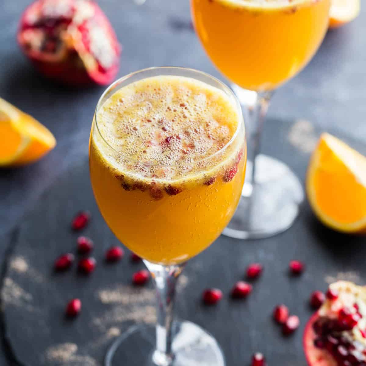 Ginger beer mimosas in wine glasses with pomegranate arils.