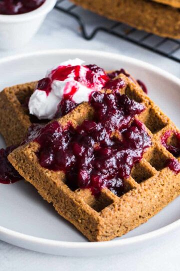 Close up of gingerbread waffles on a plate with partridgeberry compote on top.