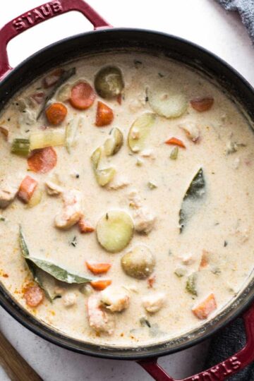 Overhead of dairy-free seafood chowder in a large pot with a wooden spoon on the side.