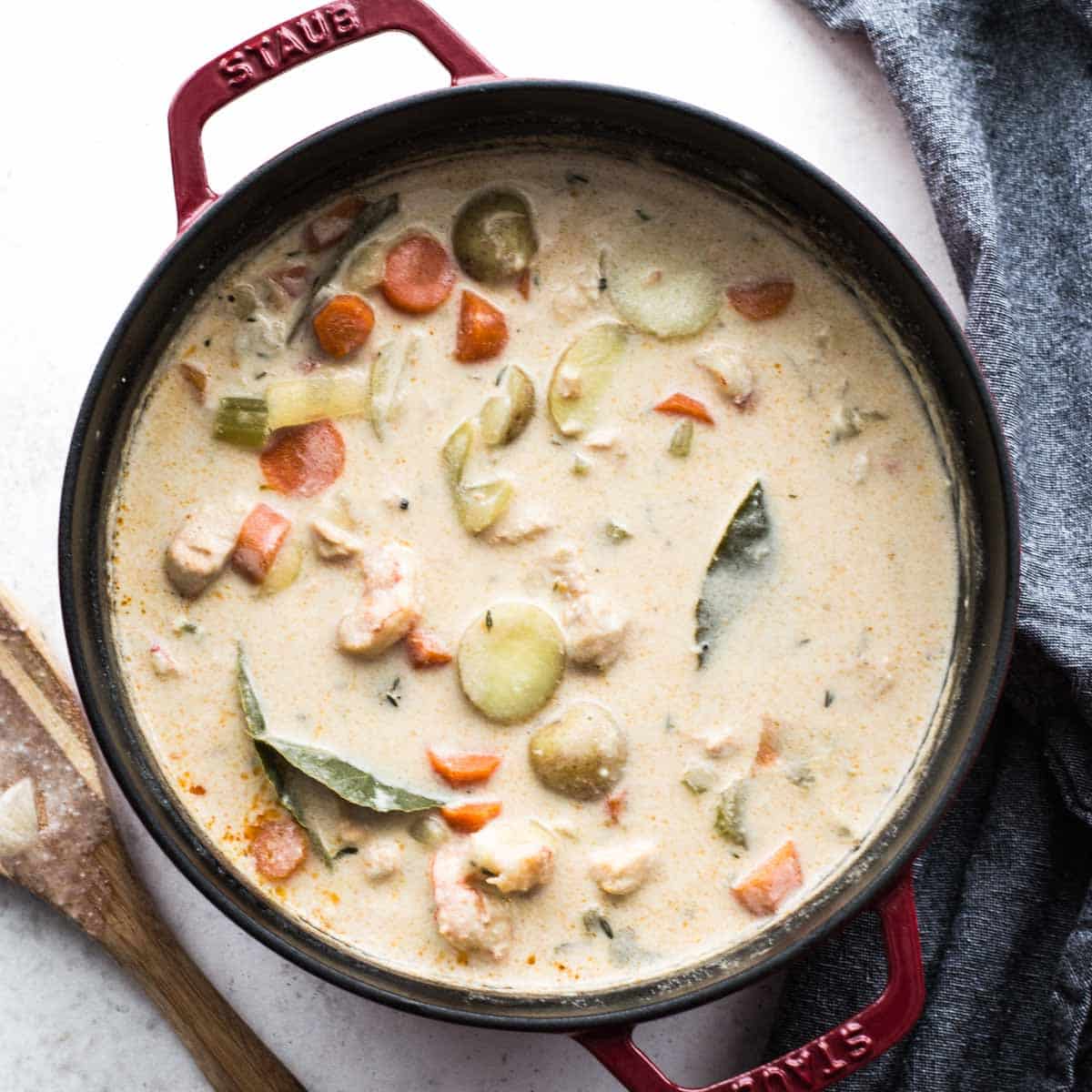 Overhead of dairy-free seafood chowder in a large pot with a wooden spoon on the side.