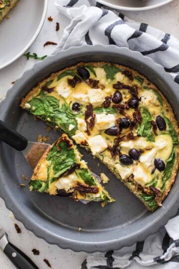 Overhead of Mediterranean quiche in a pie plate with slices removed.