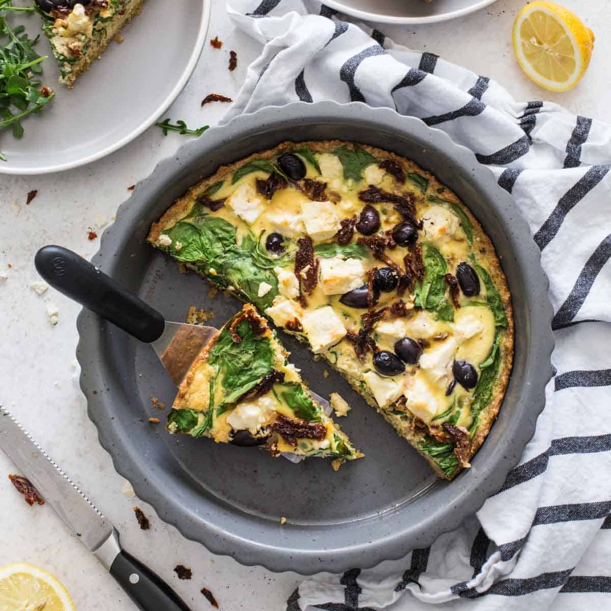 Overhead of Mediterranean quiche in a pie plate with slices removed.