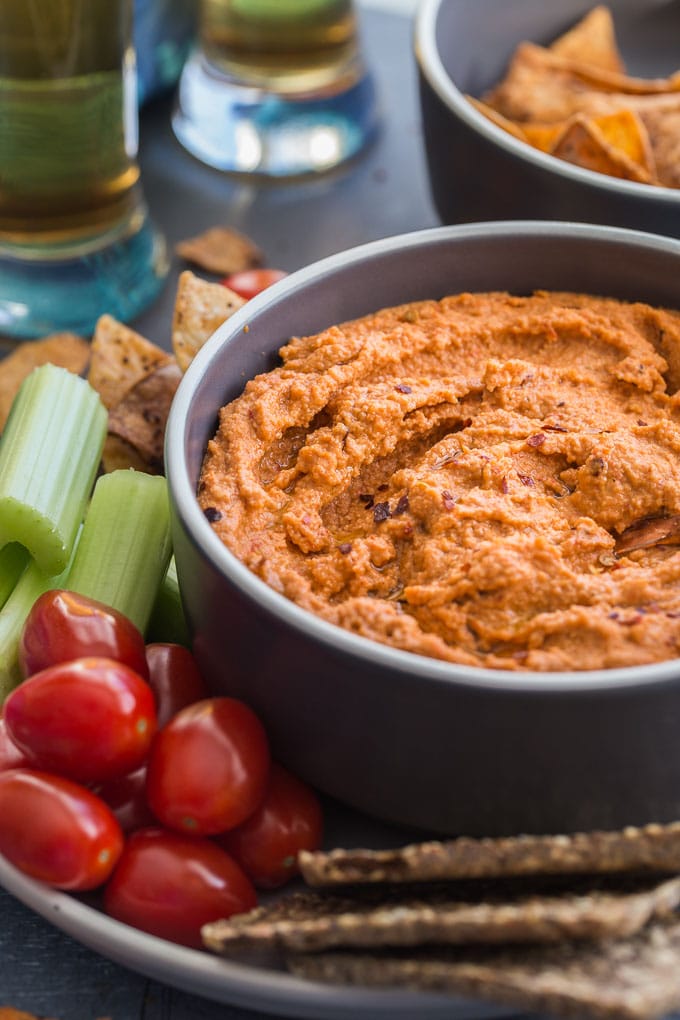 Side view of Roasted Red Pepper Cashew Dip in a bowl surrounded by veggies and crackers.
