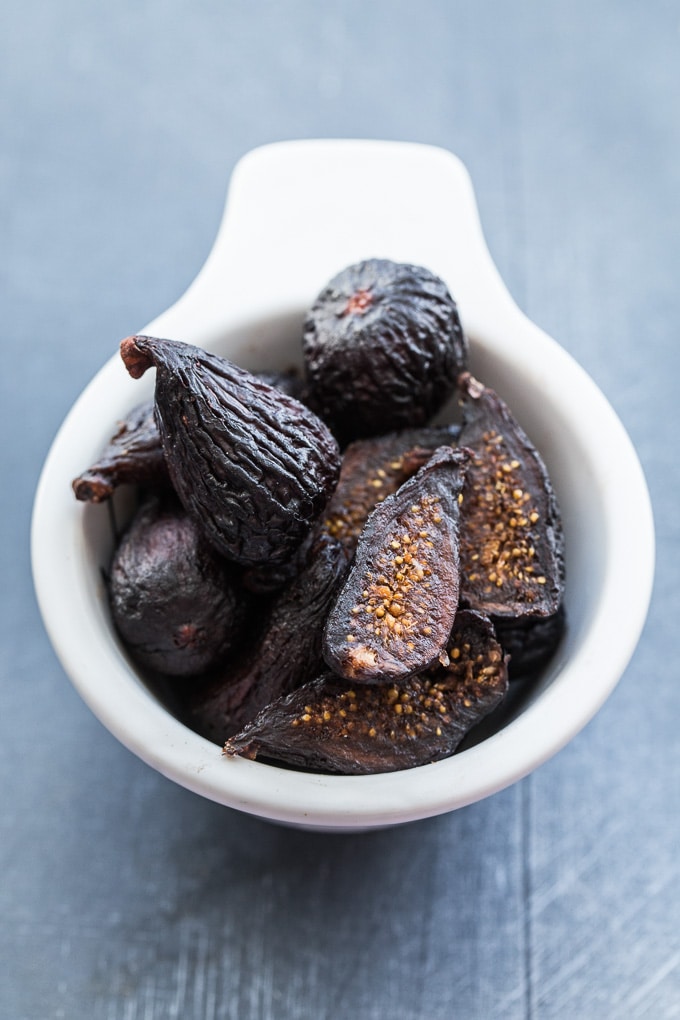 Dried mission figs in a white cup on a dark surface.