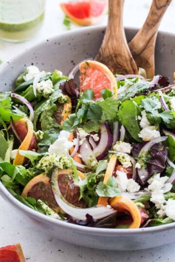 Angled view of grapefruit goat cheese salad in a grey bowl with wooden serving spoons.