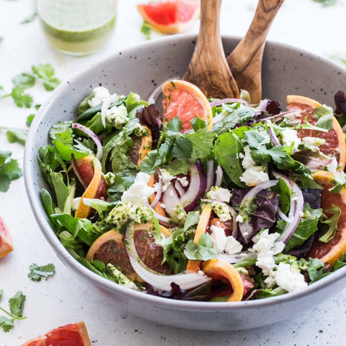 Angled view of grapefruit goat cheese salad in a grey bowl with wooden serving spoons.