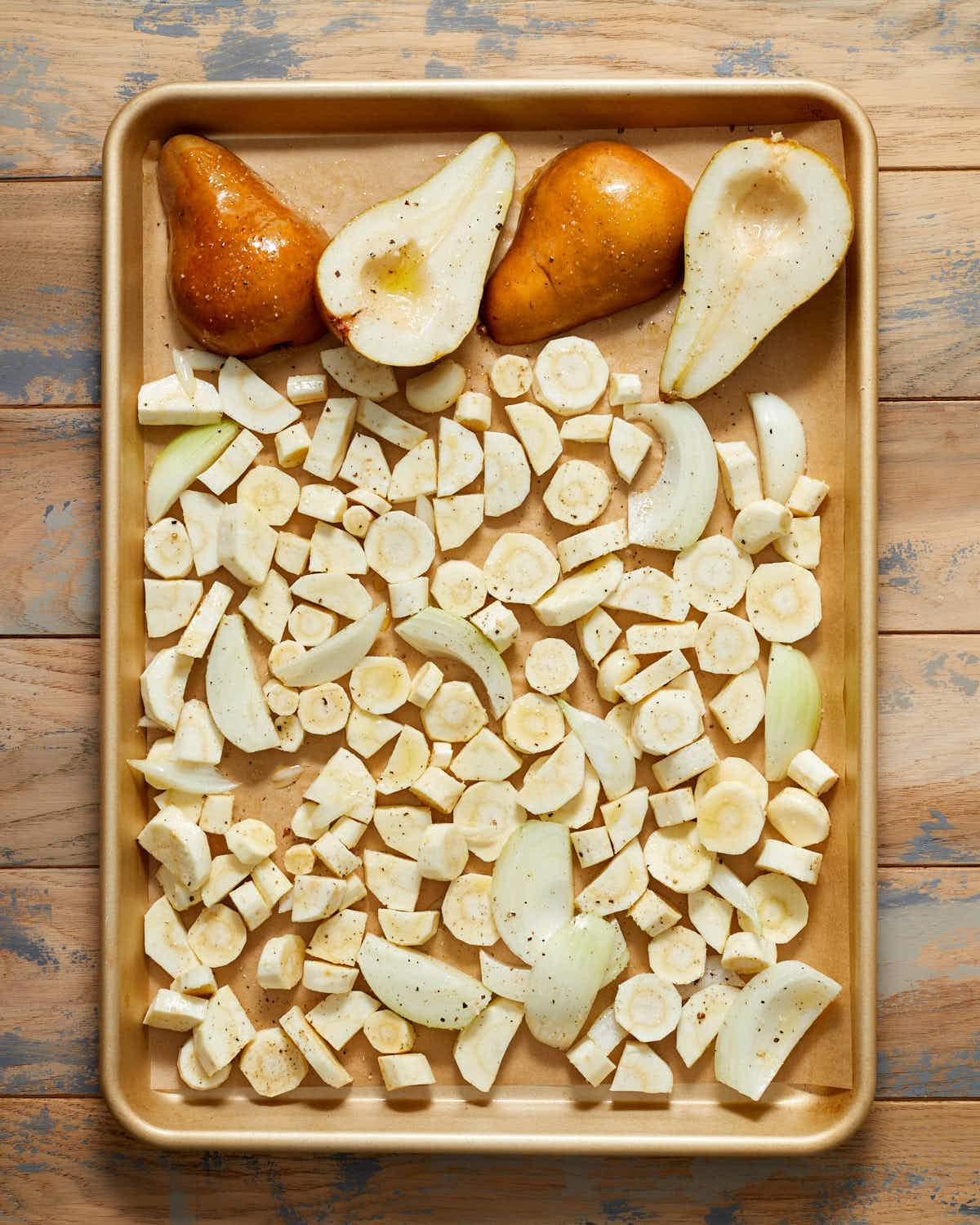 Chopped parsnip, pear halves, sliced onions and garlic arranged in single layer on a baking sheet.