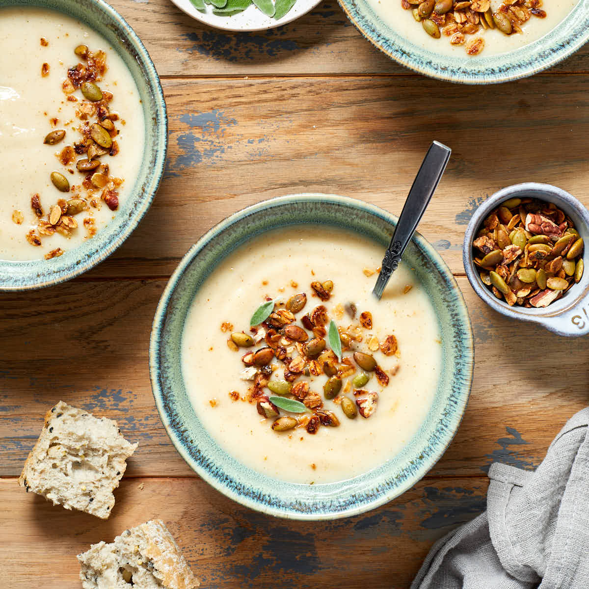 Parsnip and pear soup served in green bowls on a wooden table with savoury granola on top of the soup.