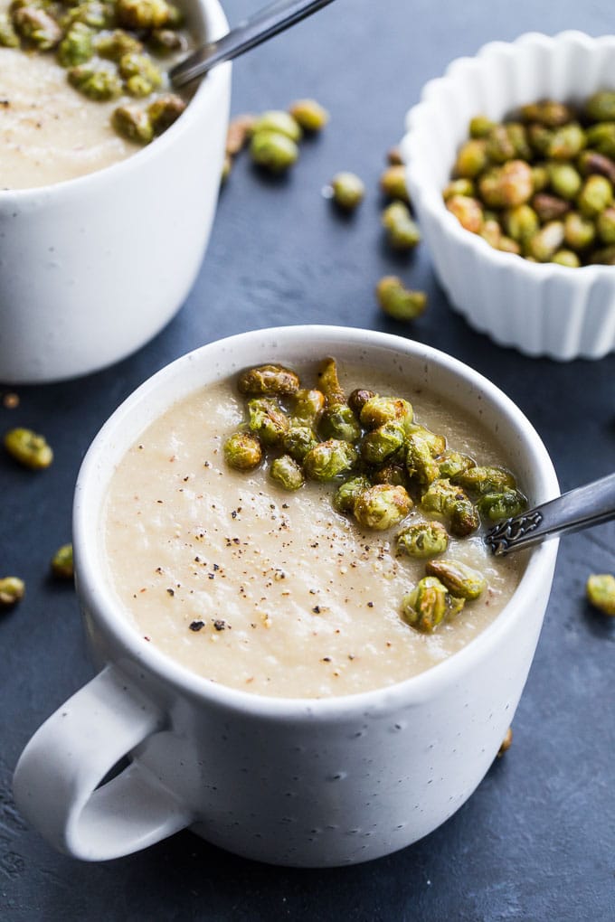 Up-close view of Roasted Pear and Parsnip Soup with Crispy Edamame in white mugs.